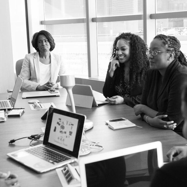 Black and white image of 3 people sat around a table with laptops in front of them during a training session